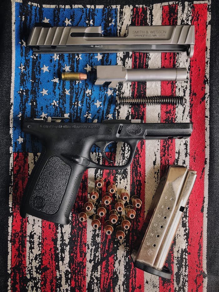 A disassembled firearm displayed on a textured American flag surface, showcasing parts and ammunition.