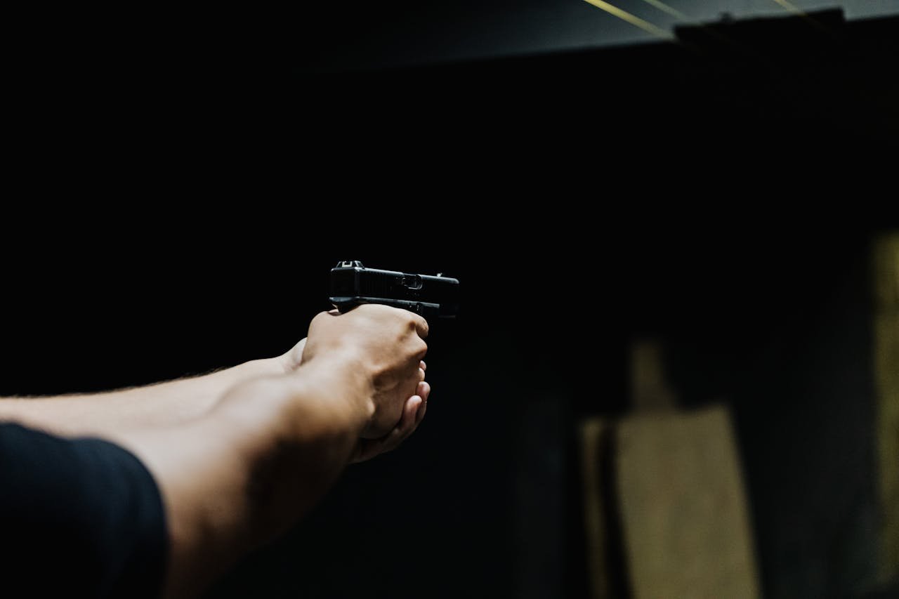 Arm aiming a handgun in a dark environment, showcasing focus and control.