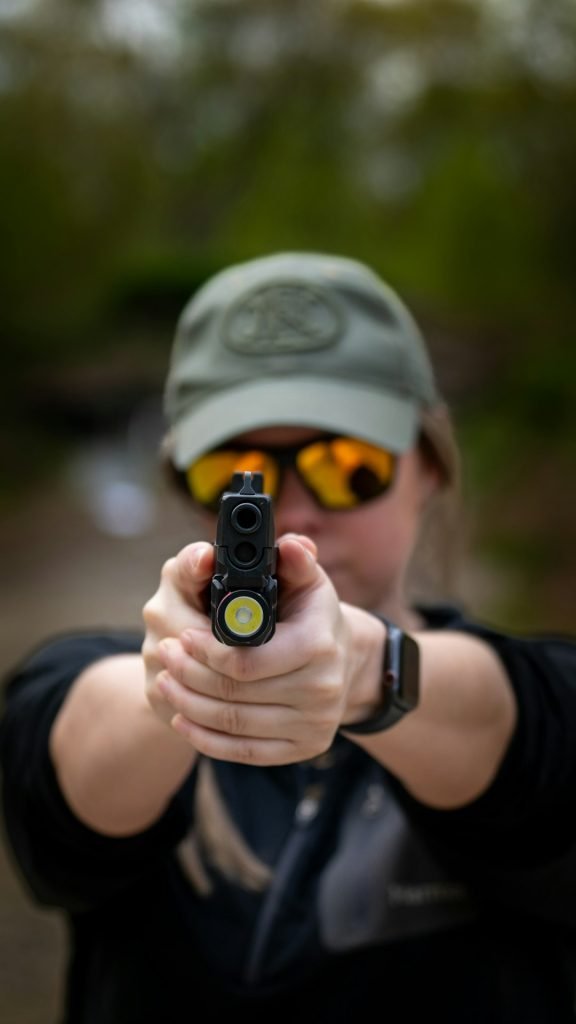 a-woman-in-a-hat-and-sunglasses-holding-a-gun-l9aqiikujg